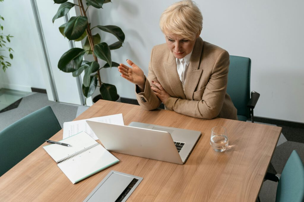 pexels photo 7222266 7222266 Professional woman in a blazer working on a laptop at a wooden desk in a modern office setting.